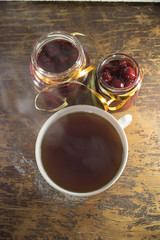 Two jars cherry jam and a Cup of tea on a wooden table. Wooden background