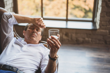 Mature businessman looking at glass with alcohol