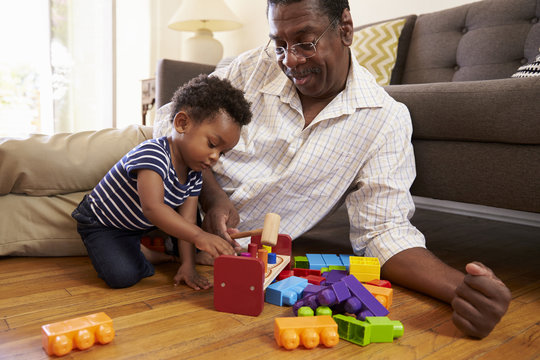 Grandfather And Grandson Playing With Toys On Floor At Home