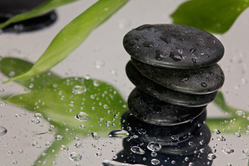 Obraz na płótnie Canvas Spa concept. Volcanic rocks and bamboo on reflective background with raindrops. Relaxation, body care treatment, wellness