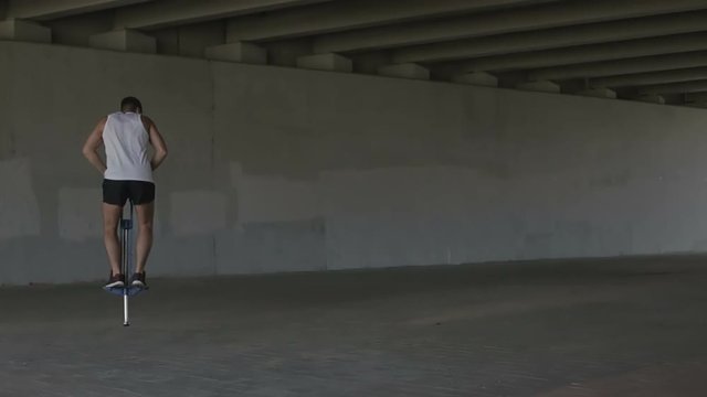 Sports guy in a shirt and shorts jumping on the spring device under a bridge.