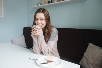 Cheerful young lady sitting in cafe and drinking coffee