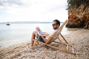 Man with his baby son at the beach, sitting on deckchair