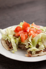 Corn tortilla tostada with refried beans, lettuce, salsa, and tomatoes with bite taken out of it
