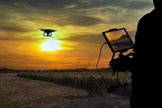 Silhouette of Man using drone to monitor the agricultural field at the evening,