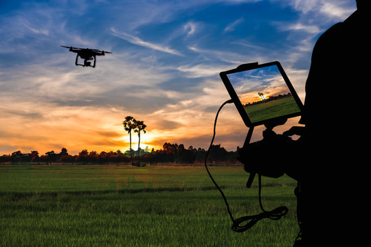 Silhouette of Man using drone to monitor the agricultural field at the evening,