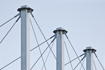 Tied Suspension Roof Cables, Three Tall Grey Masts, Cable-suspended Swooping Rooftop Pylon Anchors, Pale Blue Summer Sky, Large Detailed Horizontal Closeup, Contemporary Construction Concept