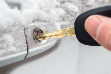 Close-up of a key inserted into the lock of frozen car door in winter