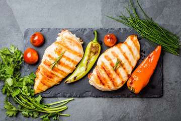 Grilled chicken fillets, chili and tomatoes on black slate plate