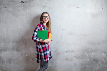 Portrait of a happy young student in checkered shirt with colorful books on the gray wall background