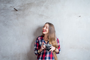 Portrait of young female photographer with retro camera on the gray wall background