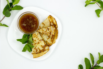 Crepes on a white plate with mint leaves and a Cup of honey