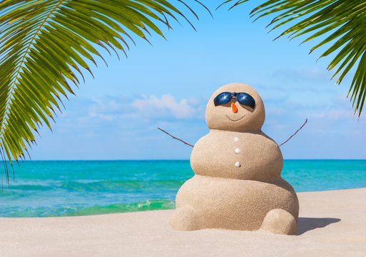 Positive sandy snowman in sunglasses at palm ocean sandy beach