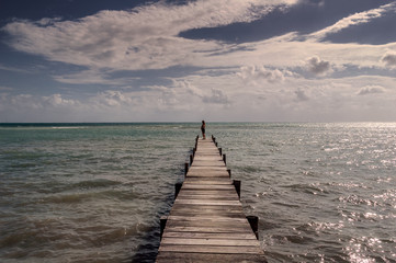 Fototapeta premium Samotna kobieta na końcu długiego nabrzeża spoglądająca na ocean