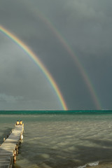 Double rainbow on stormy tropical sky watched by people on a wharf