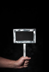 Hand hält leeres Hinweisschild vor schwarzem Hintergrund