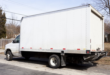 Rear and side views of white delivery van parked on residential neighborhood street. Horizontal.