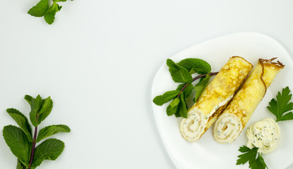 Crepes with cheese sauce on a white plate with mint leaves