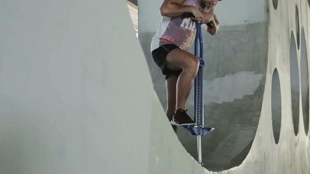 Bottom view. Muscular young athlete stands in a round hole in the concrete wall and is preparing to jump on spring stick.