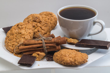 Still life with Cup of coffee, biscuits, chocolate and cinnamon on a white plate.