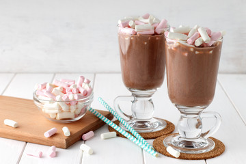 Glasses of hot chocolate with marshmallows on white wooden table.