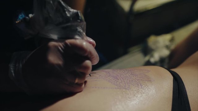 Close-up of hands of tattoo artist in gloves tattooing a pattern on body macro 4K