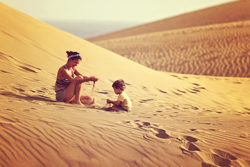 Mother with son playing with sand in a desert in Gran Canaria