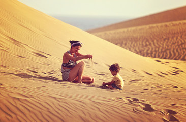 Fototapeta na wymiar Mother with son playing with sand in a desert in Gran Canaria