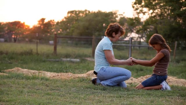 A woman and her granddaughter kneeling in a field praying together.