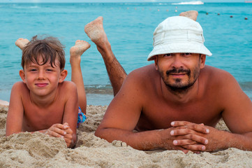 Father and son lying on the sand on the beach