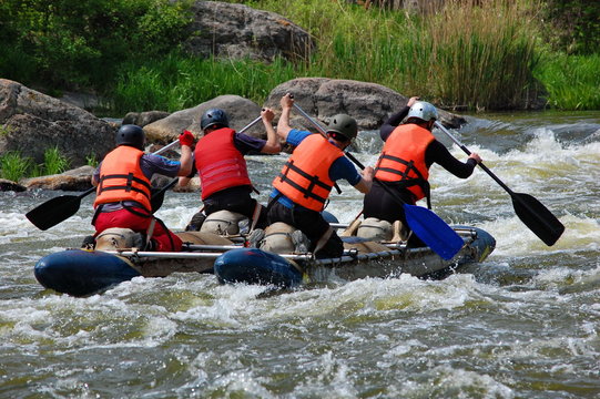 Team of  athletes on an inflatable catamaran row up the stream in a thresholds. Southern Bug river, Ukraine.
