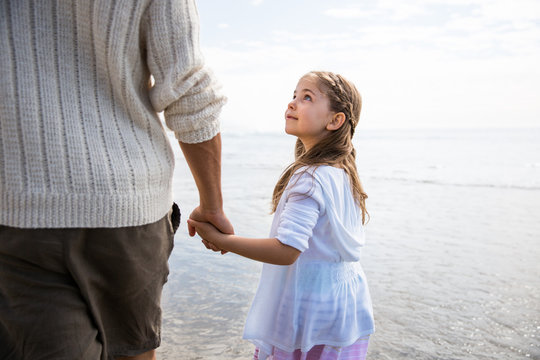 Father and daughter holding hands on a beach. Girl looks up towards father. California