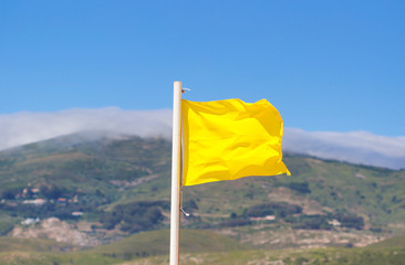 Yellow flag waving on the beach in the breeze against a blurred blue sky.