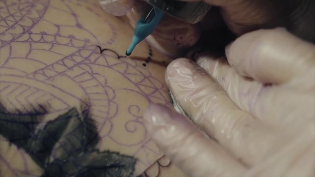 Close-up of hands of tattoo artist in gloves tattooing a pattern on body macro HD