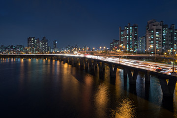 Lit residential district along the Han River and traffic on a bridge in Seoul, South Korea, at night.