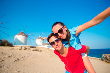 Young couple taking selfie with a stick in front of windmills at popular tourist area on Mykonos island, Greece