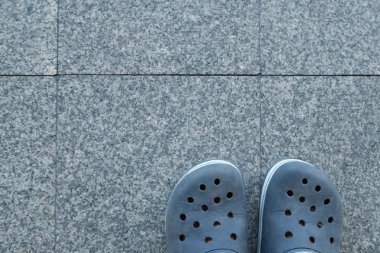 Feet in sandal on pavement background, top view.