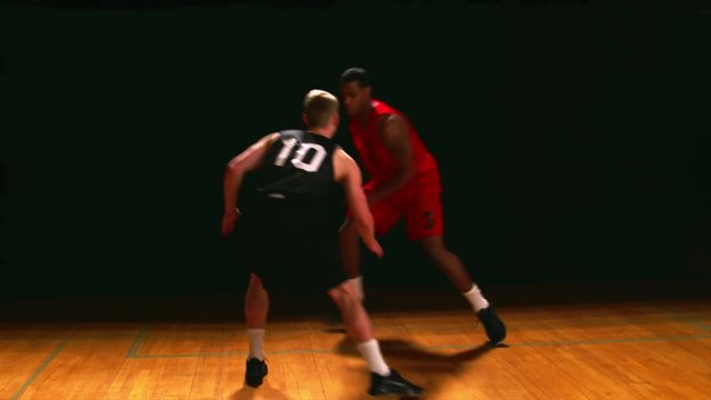 A basketball player defends an opponent, against a black backdrop