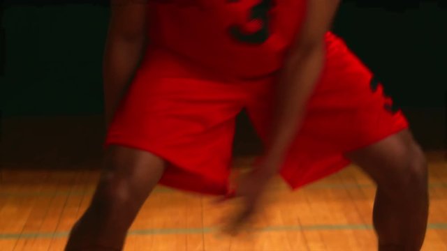 A basketball player dribbles the ball between his legs, against a black backdrop, close up