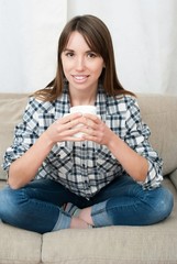 woman sitting on couch in her living room and drinking coffee