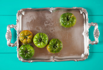 green heirloom tomatoes on silver tray on Iris Blue background © irynagrygorii