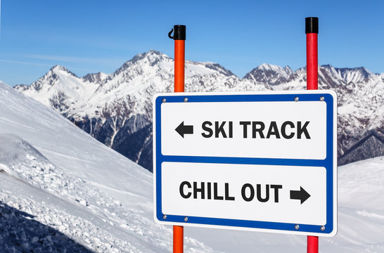 Ski track and chill out dilemma sign with arrows showing opposite directions against snowy mountain and blue sky winter background