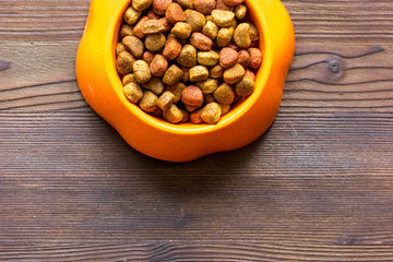 dry cat food in bowl on wooden background top view
