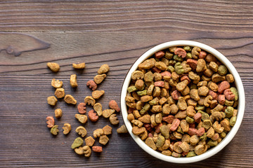 dry cat food in bowl on wooden background top view