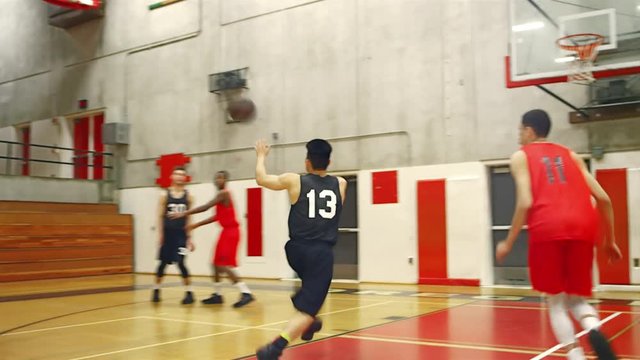 Basketball players passing the ball down the court during a game and making a basket