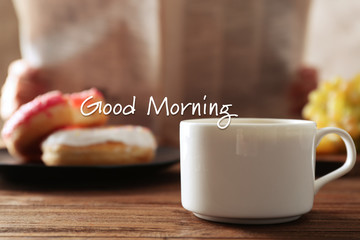 Cup of aromatic drink on table. Text GOOD MORNING on background