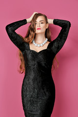 Fototapeta premium Portrait of gorgeous young woman in black evening gown on pink background