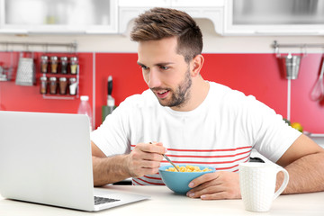 Young man having breakfast while working with laptop in kitchen