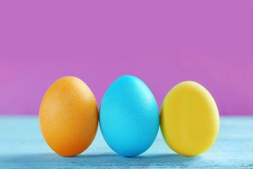 Easter eggs on wooden table against color background