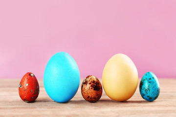 Easter eggs on wooden table against color background